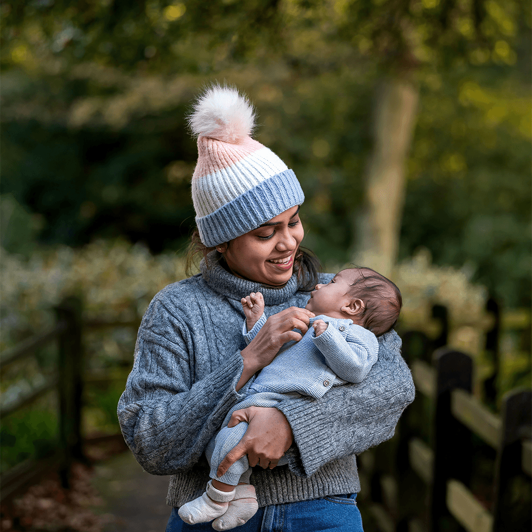 Mother in a knit hat holding her newborn outdoors