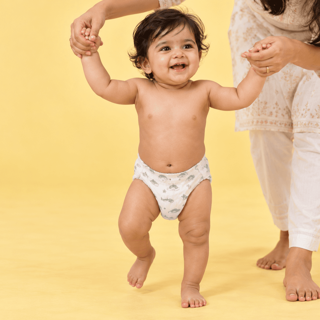 Baby taking first steps holding a parent's hand, wearing a Lumi9 diaper